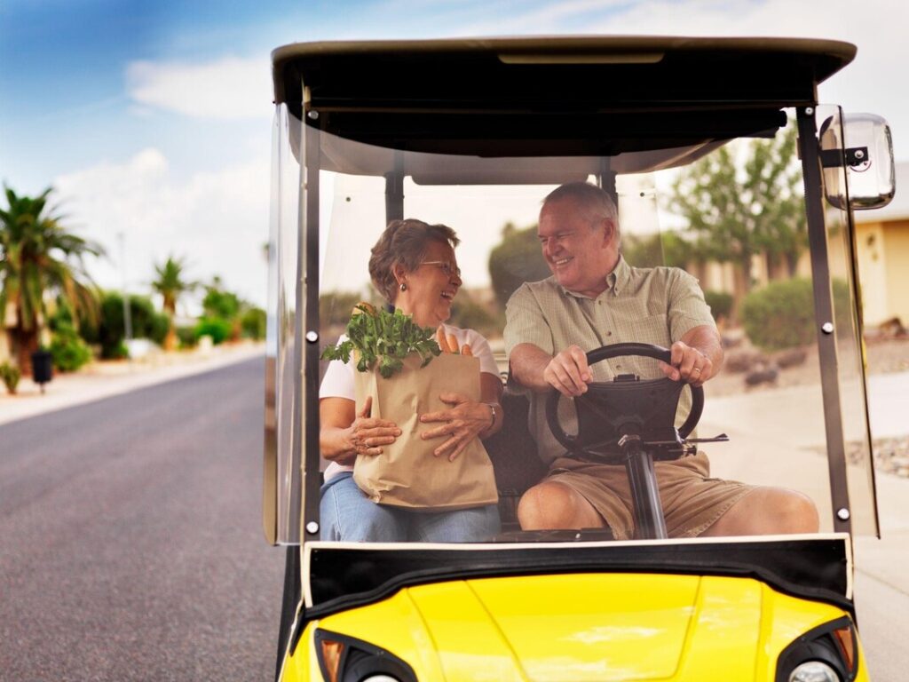 Happy senior couple riding yellow Anna Maria Island golf cart rental with groceriesPicture