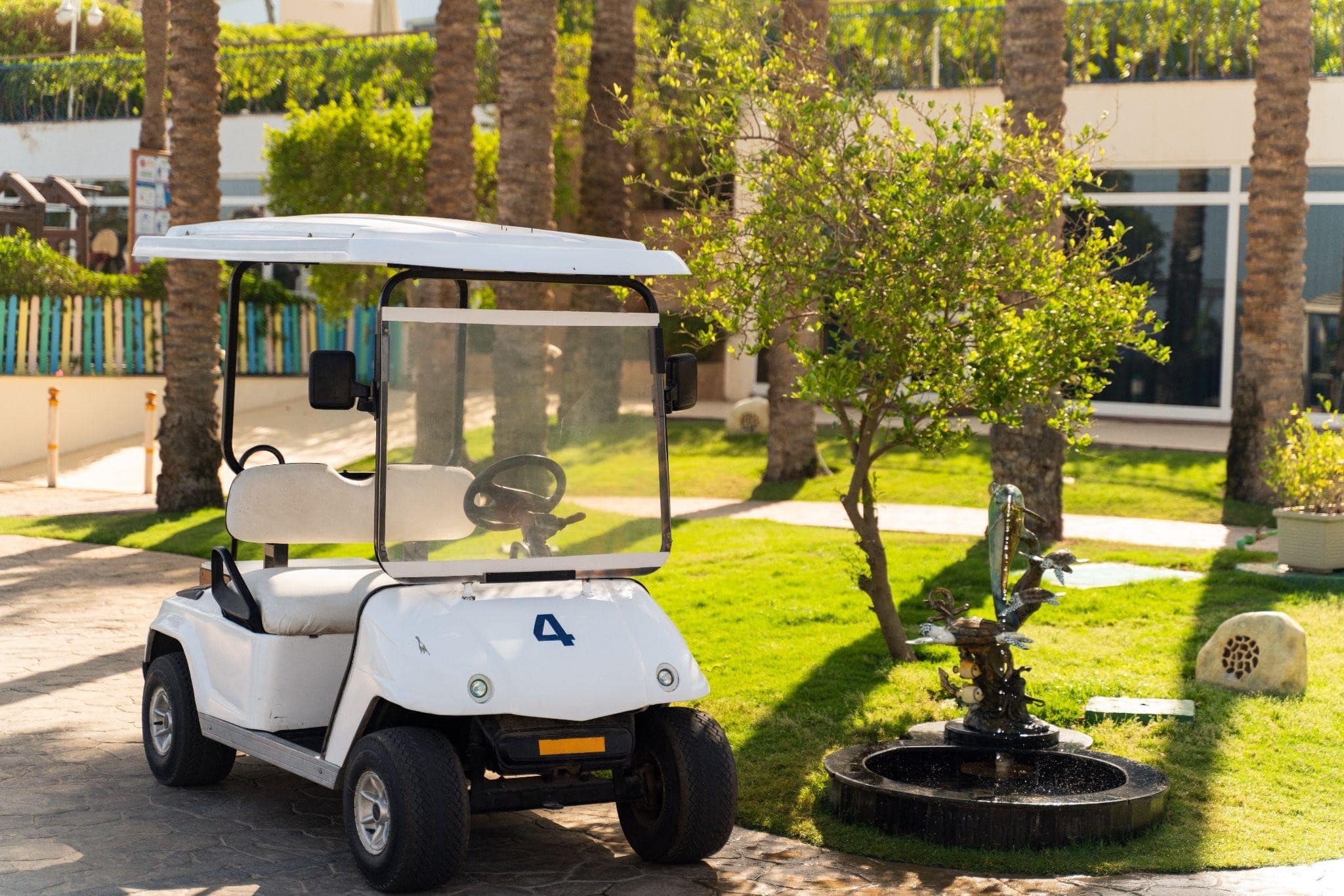White electric golf cart rental parked neatly near a resort fountain, illustrating stress-free golf cart rentals near me on Anna Maria Island.