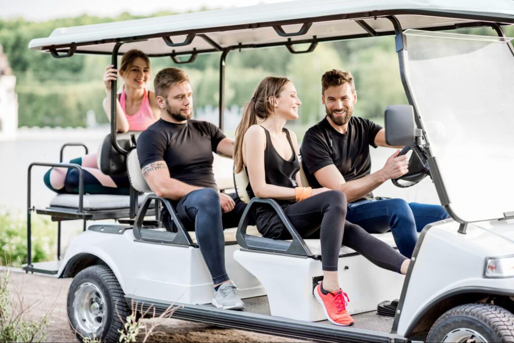 Group of friends laughing and riding together in a 6-passenger golf cart on a sunny day.